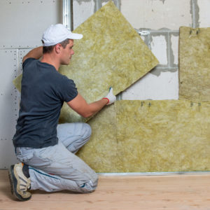 Worker insulating a room wall with mineral rock wool thermal ins Worker insulating a room wall with mineral rock wool thermal insulation.